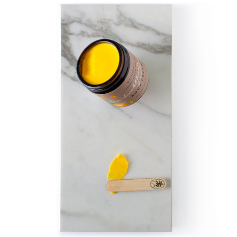 1. Flat lay of BONOBO Sea-Buckthorn and Calendula Body Cream with open jar and cream on spatula, showcasing vibrant yellow color