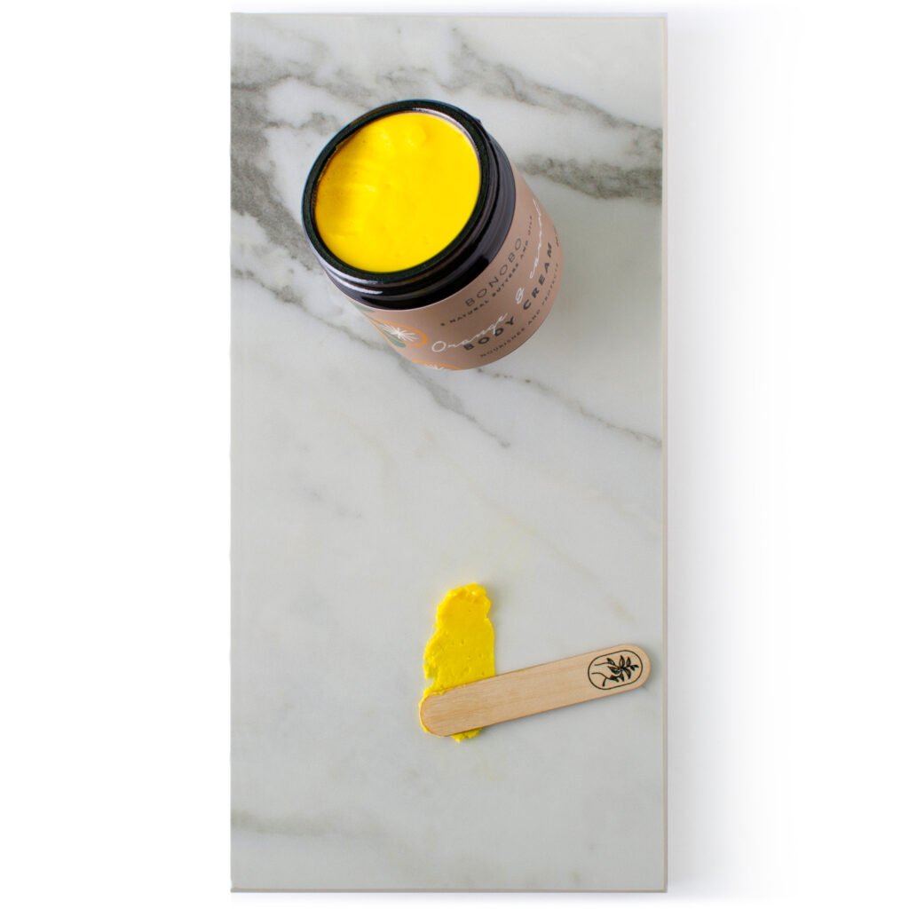 4. Close-up of BONOBO Orange & Carrot Body Cream with vibrant yellow texture and wooden spatula on marble surface