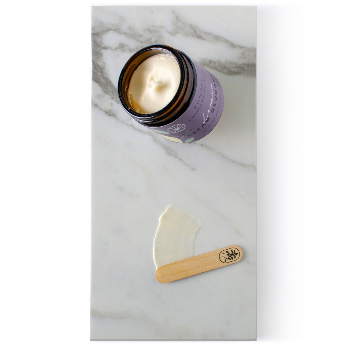 2. Open jar of BONOBO Lemon Deodorant-Cream with cream and applicator on marble surface