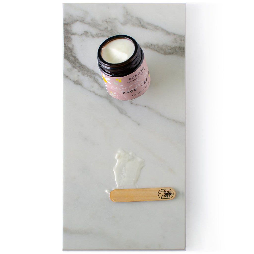 4. Open jar of BONOBO Chamomile & Lady’s Bedstraw Face Cream with handcrafted juniper spatula on marble