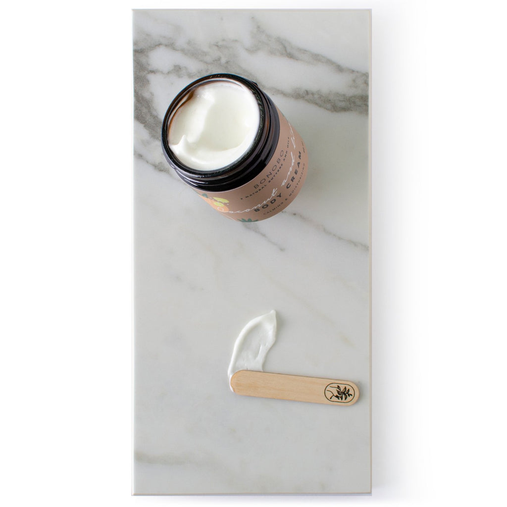 2. Flat lay of BONOBO Coconut and Lime Body Cream jar with cream on a spatula, displayed on marble