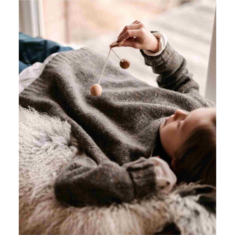 1. Child lying on a cozy blanket playing with Wooden Story Bon Bon Ball toy, holding it above with one hand