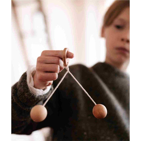 1. Close-up of child holding Wooden Story Bon Bon Ball toy by the handle, focusing on the wooden balls and string