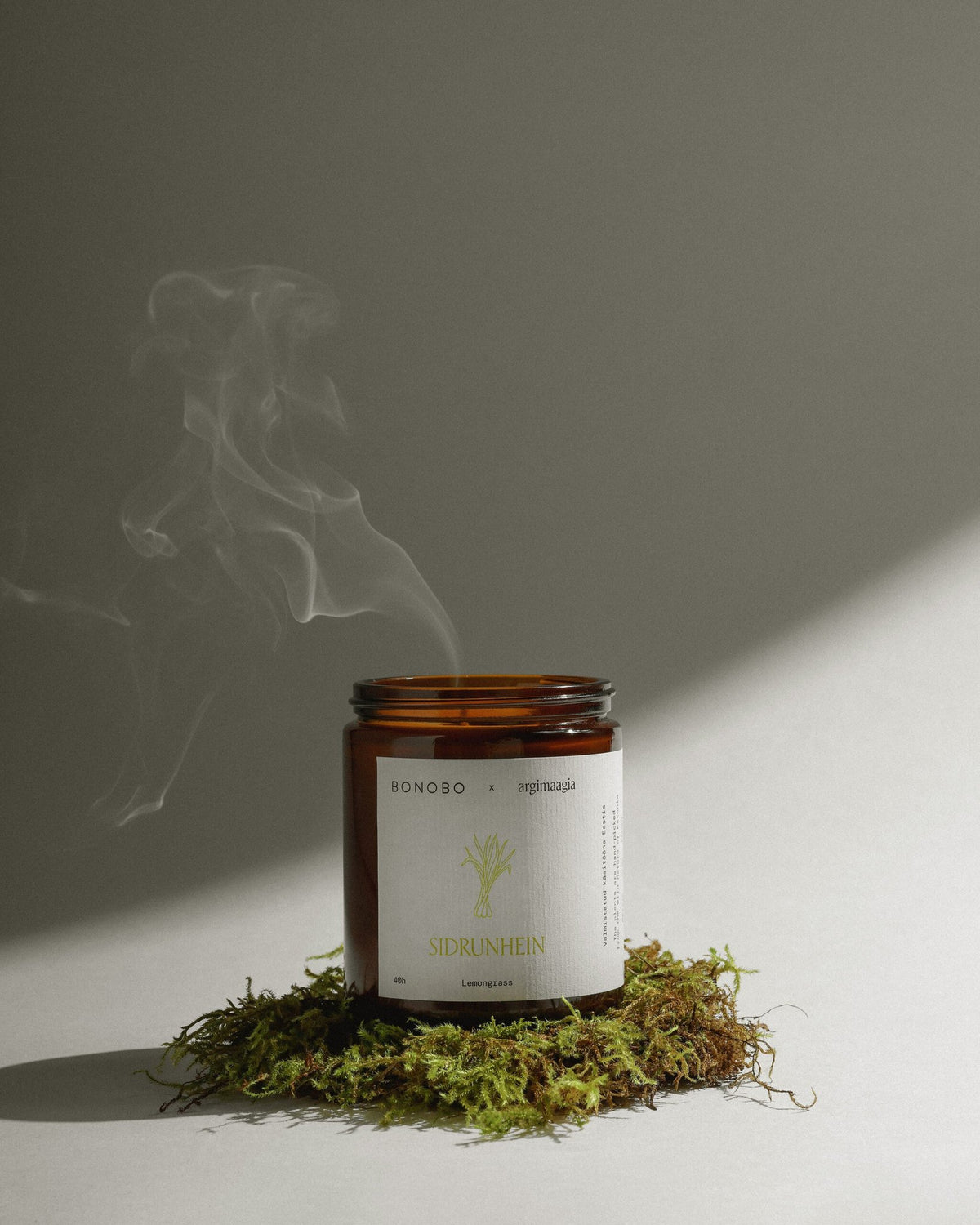 1. Bonobo lemongrass scented candle in amber glass jar with smoke rising, placed on moss, showcasing natural and eco-friendly design