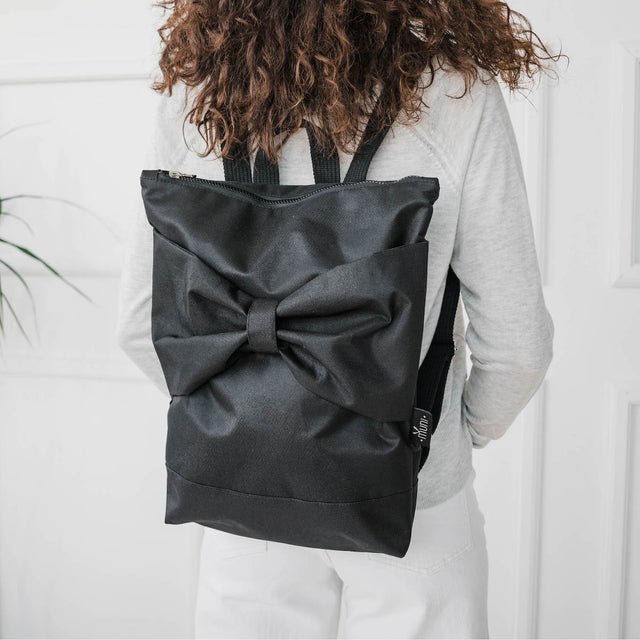 4. Woman wearing Muni Black Bow backpack indoors, showing adjustable straps and large bow detail