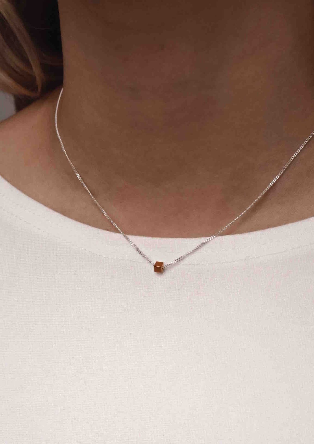 1. Woman wearing NO MORE gold box necklace with sterling silver chain against a white top