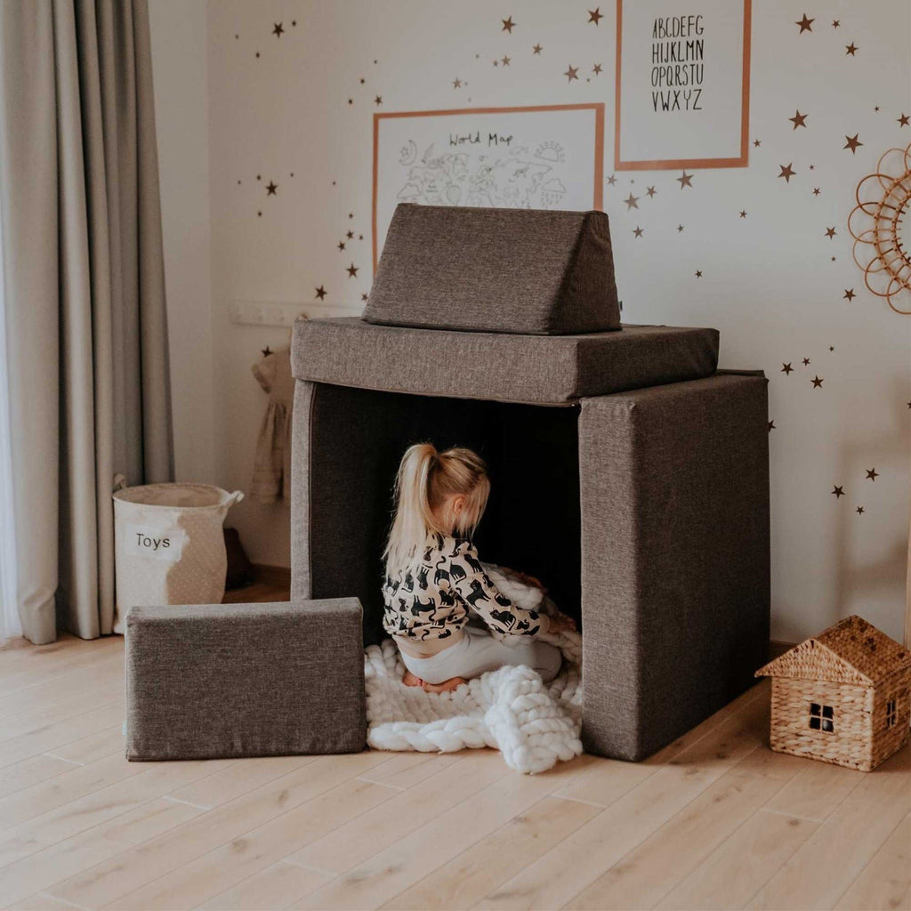 3. Child sitting inside a fort made from Monboxy dark brown play mattress set in a decorated room