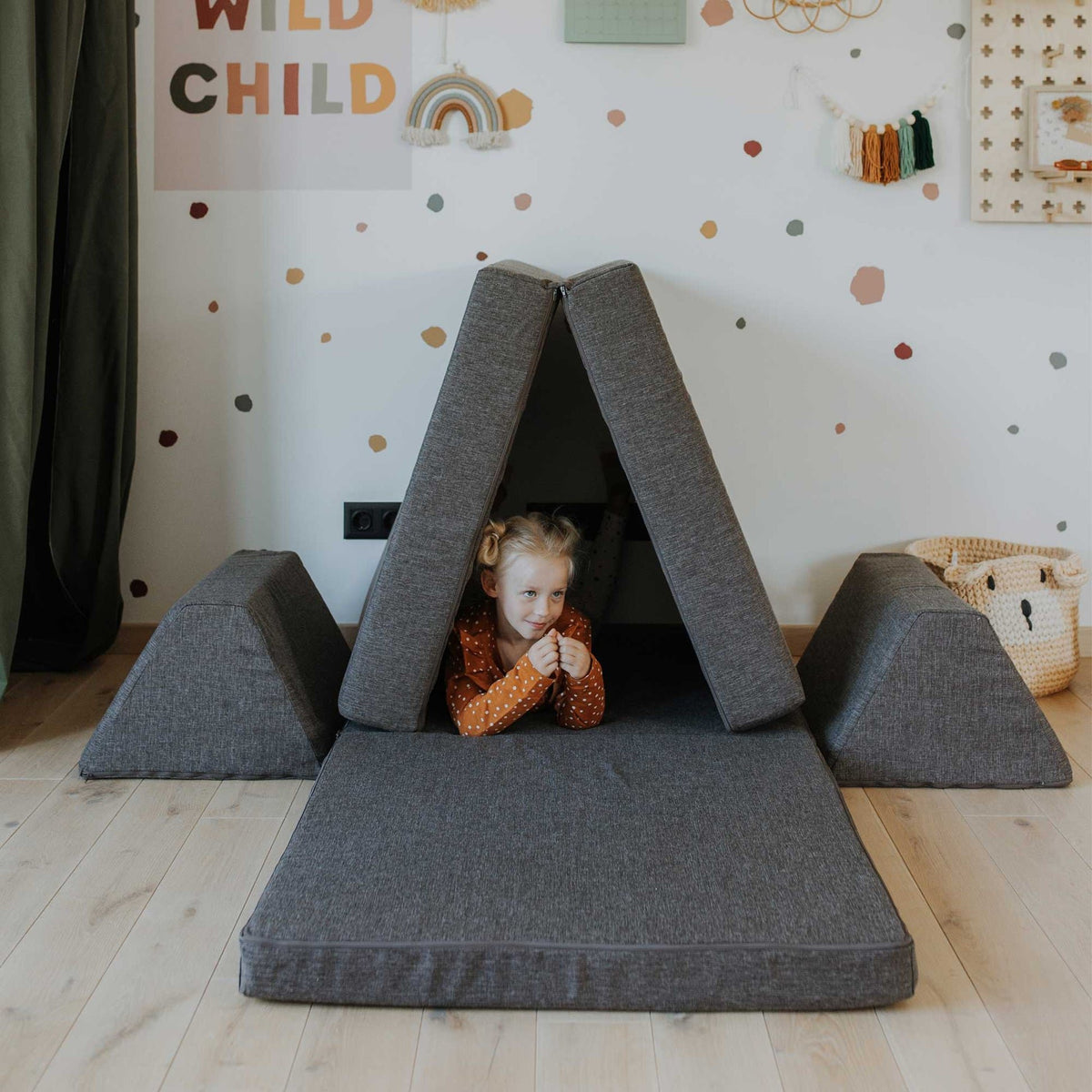 5. Child peeking out from a tent made with Monboxy dark brown play mattress set in a playroom