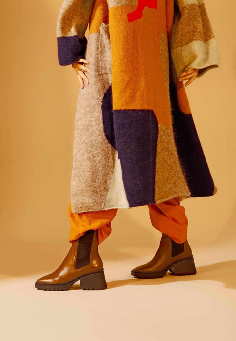 1. Person wearing brown calf leather combat boots with 7.8 cm heel, styled with colorful coat and orange pants in lifestyle setting