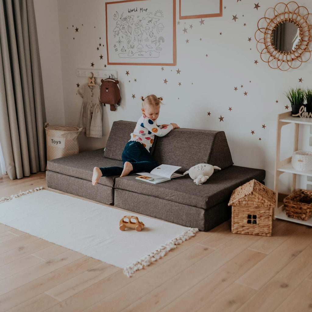 9. Child sitting on Monboxy dark brown play mattress set configured as a sofa in a playroom