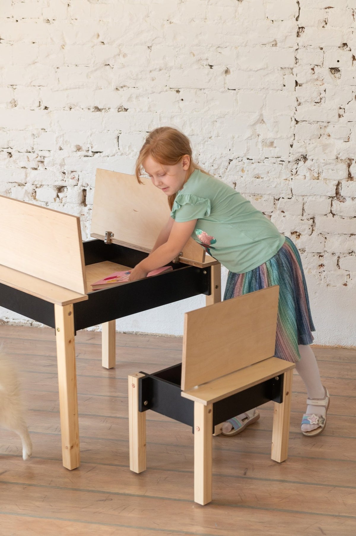 7. Girl using black and natural wood table and chair set with open storage in a room with white brick wall