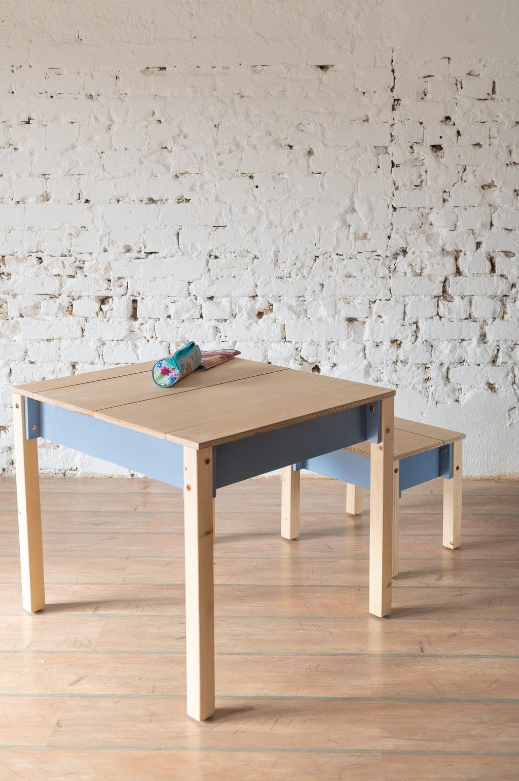 5. Blue and natural wood children's table and chair set with closed storage in a room with white brick wall