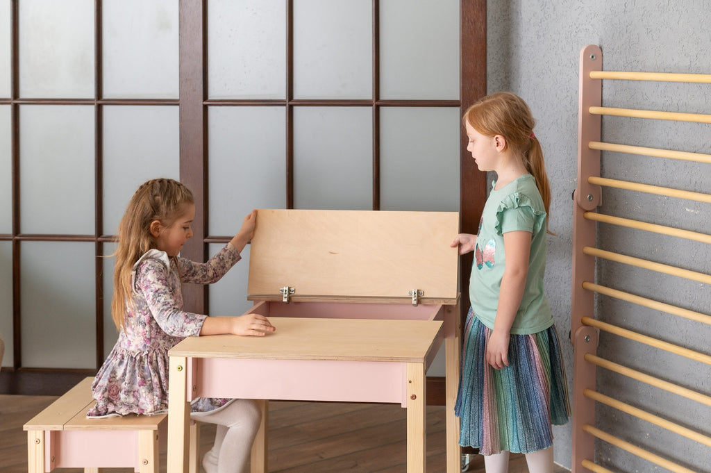17. Two girls interacting with pink and natural wood table and chair set in a room with wooden floor and gym ladder