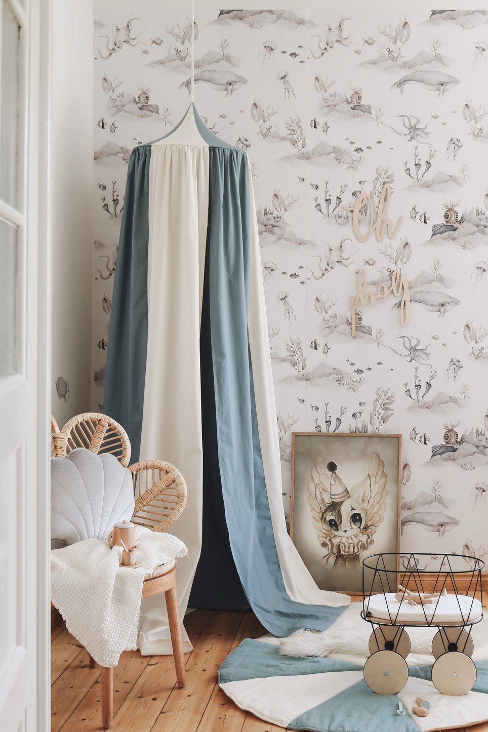 8. Blue and cream canopy in a nursery with whimsical wallpaper, wooden flooring, and decorative items