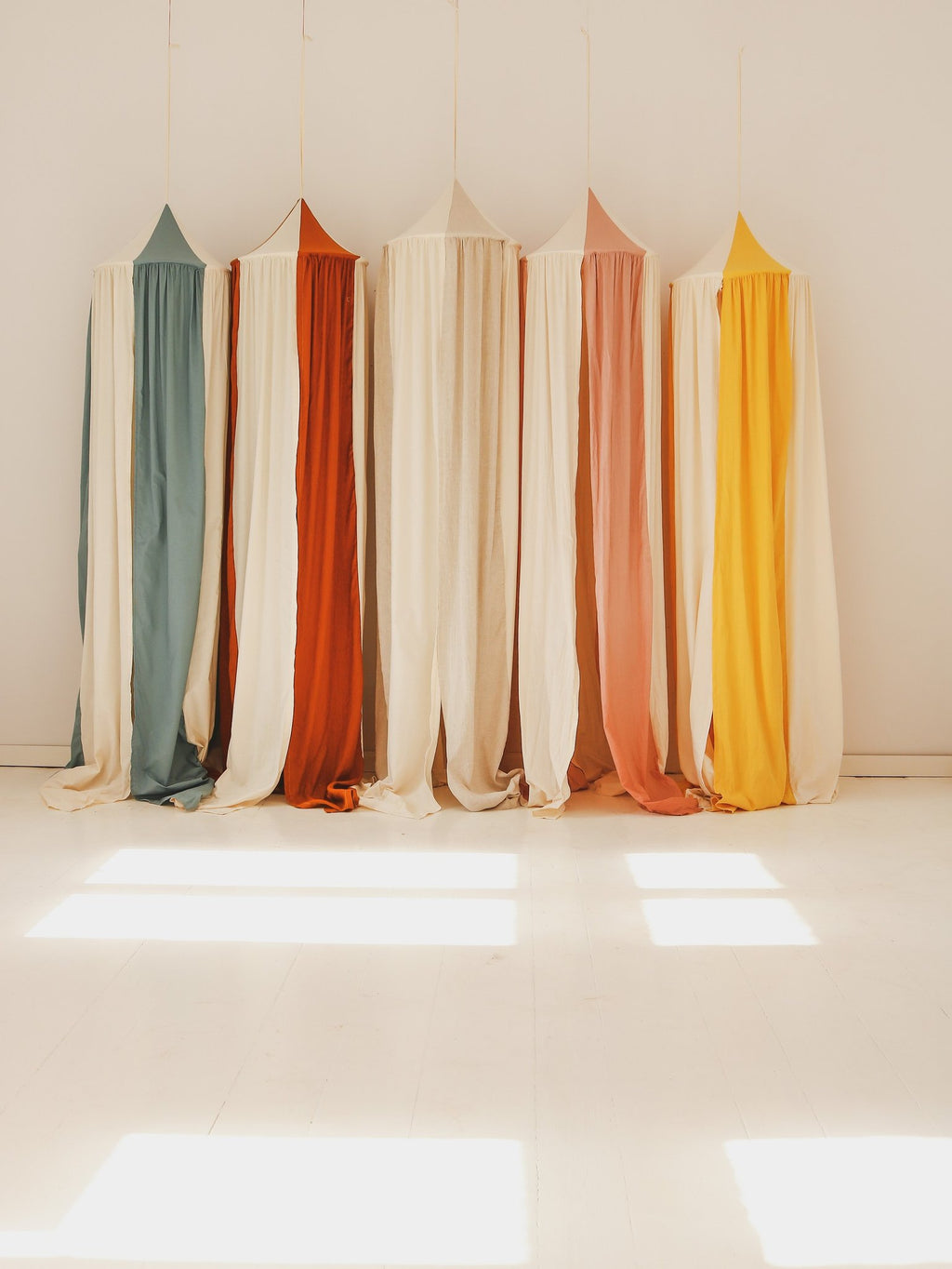 4. Five canopies in various colors including blue, orange, pink, and yellow hanging in a sunlit room