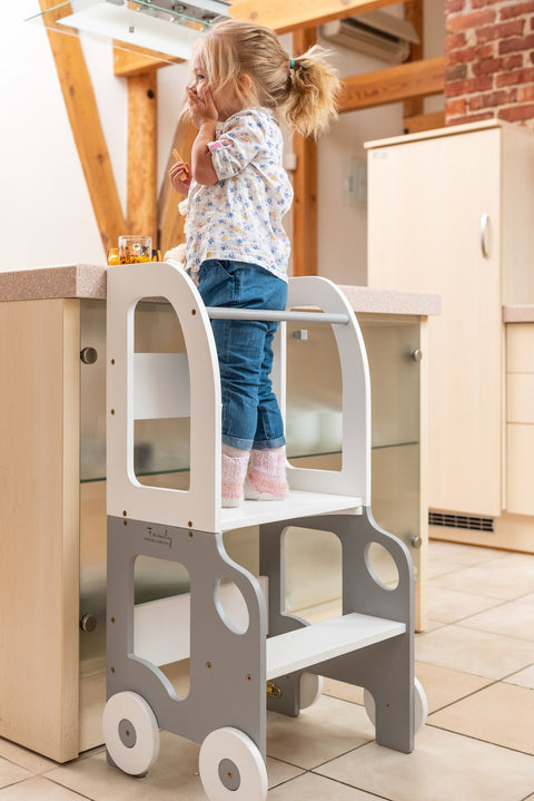 1. Child standing on grey and white Montessori kitchen step stool at a kitchen counter