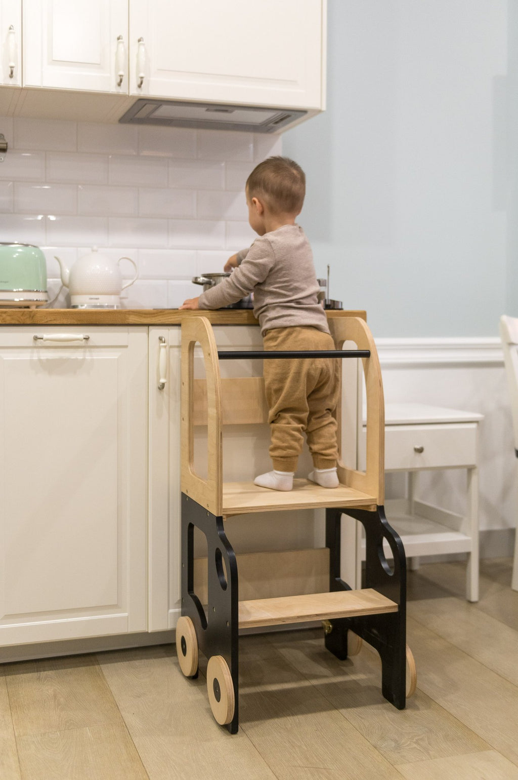 1. Child using black and natural wood Montessori kitchen step stool at kitchen counter