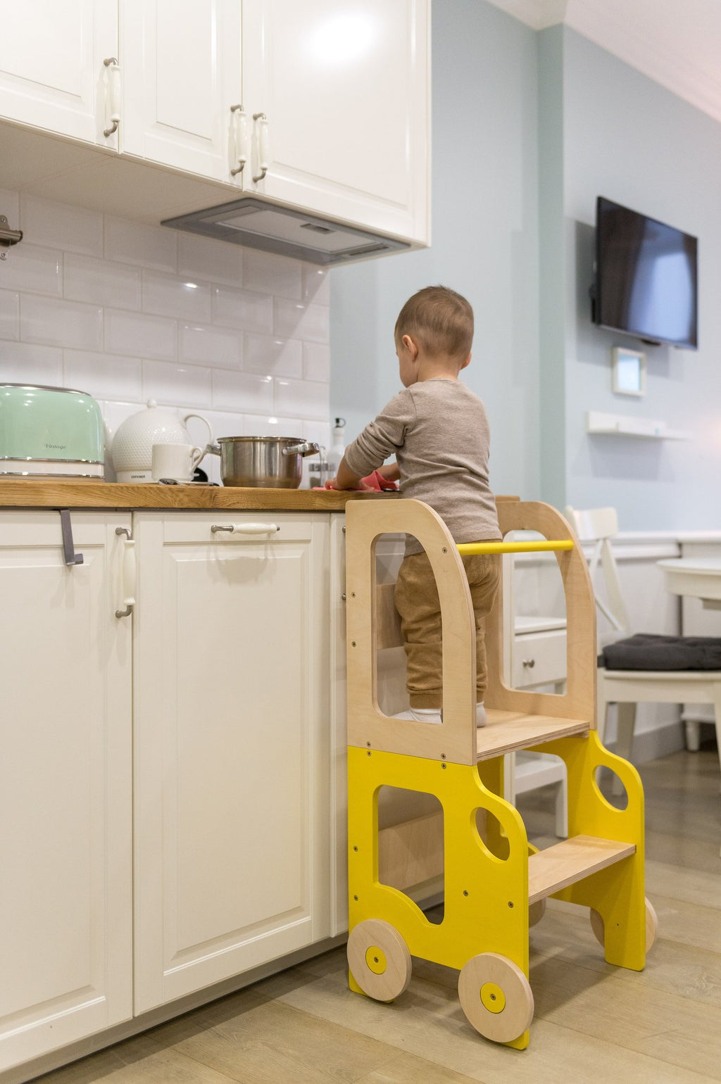 1. Child using yellow and natural wood Montessori kitchen step stool at kitchen counter
