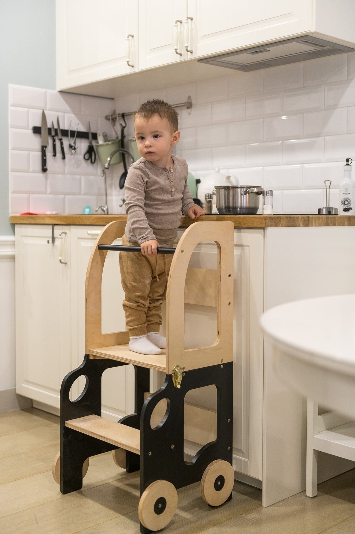 1. Child using black and natural wood Montessori kitchen step stool at kitchen counter
