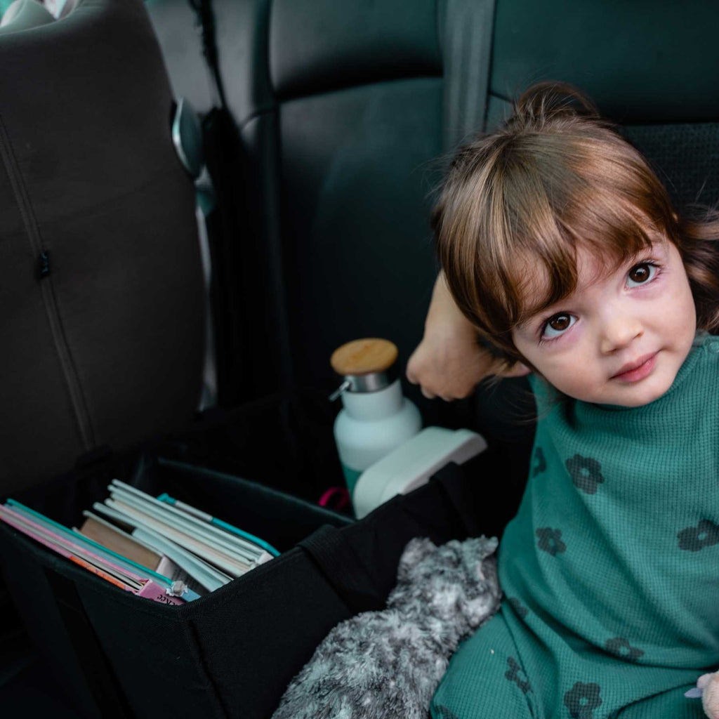 1. Young girl sitting in car with black Ezimoov organizer bag filled with books and a water bottle