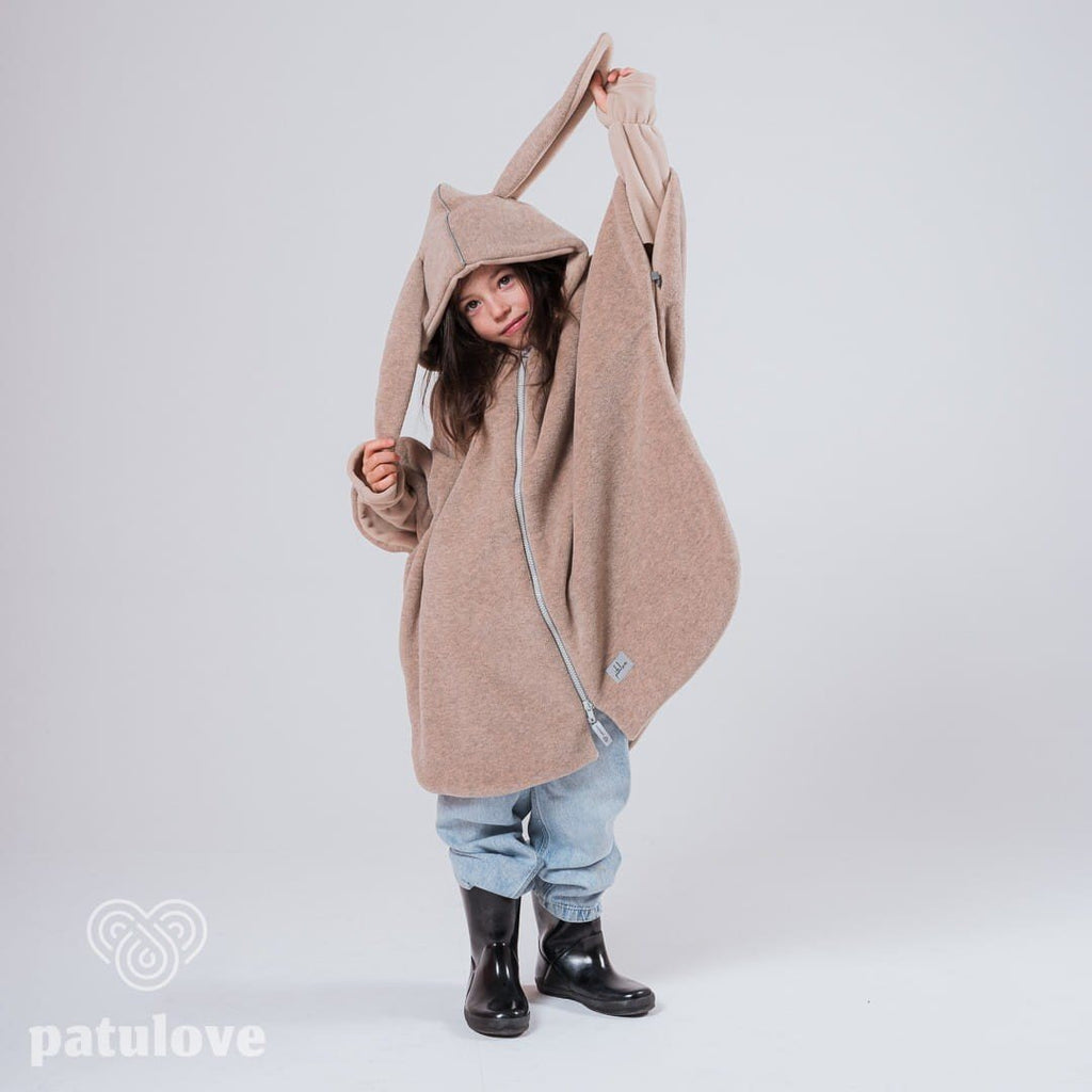 4. Child wearing Patulove beige bunny car poncho with hood, playfully holding ear in studio