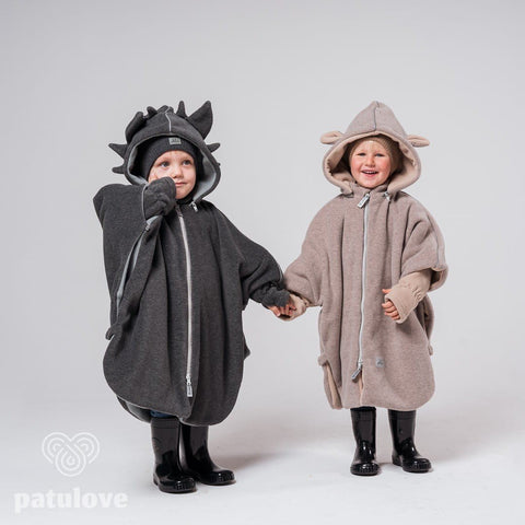 3. Two children wearing Patulove car ponchos, one dragon-themed and one bunny-themed, holding hands in studio setting