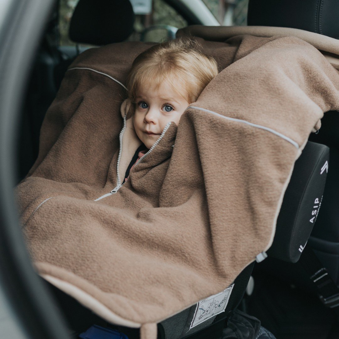 3. Toddler in car seat covered with brown Patulove car poncho, showing magnetic fasteners