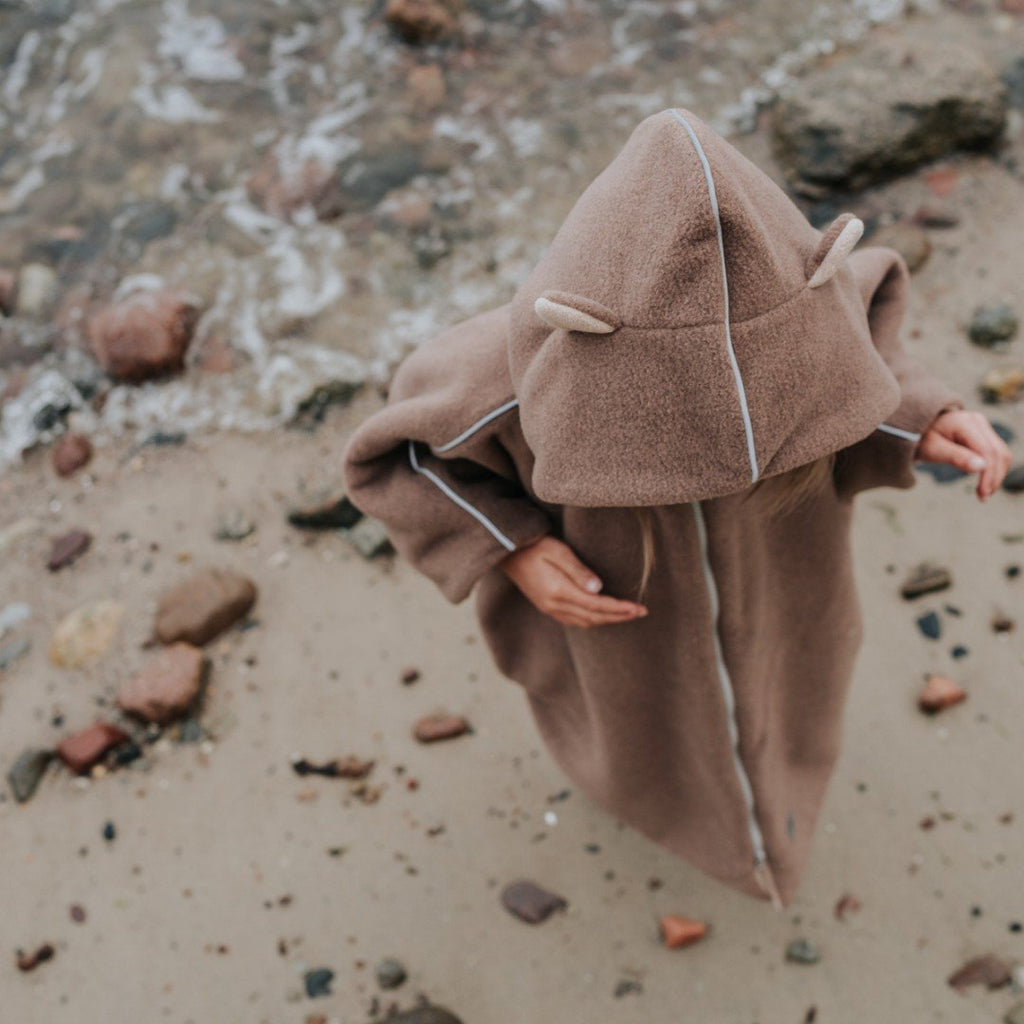 7. Child wearing brown Patulove car poncho with hood, walking on rocky beach