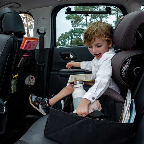 1. Child sitting in car with Ezimoov car seat organizer holding books and water bottle