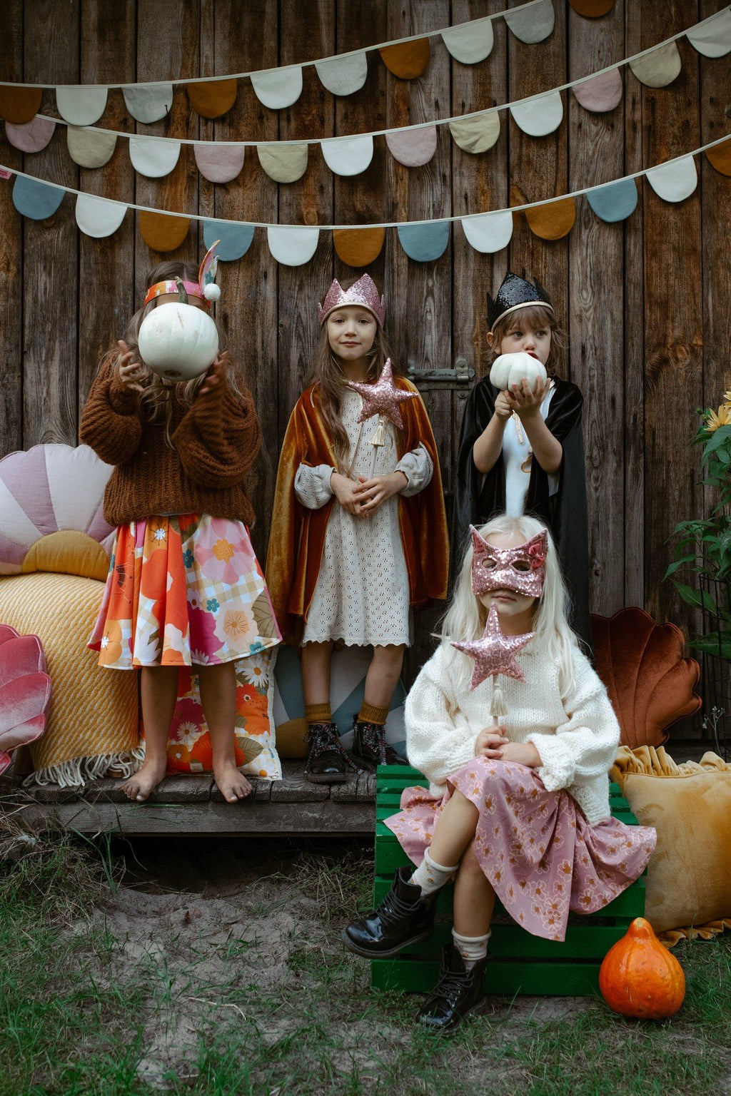 11. Four children in costumes, one wearing a black cat mask, holding pumpkins in a rustic setting