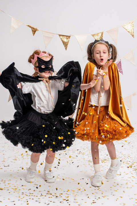 5. Two children in costumes, one with a black cat mask, celebrating with confetti under bunting