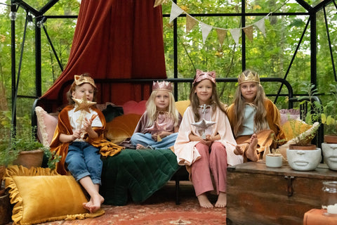 1. Four children in costume, one wearing gold sequin cat mask, sitting in a decorated greenhouse