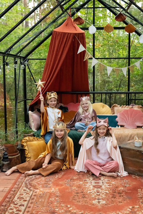 1. Four children in costume, one wearing gold sequin cat mask, posing in a decorated greenhouse