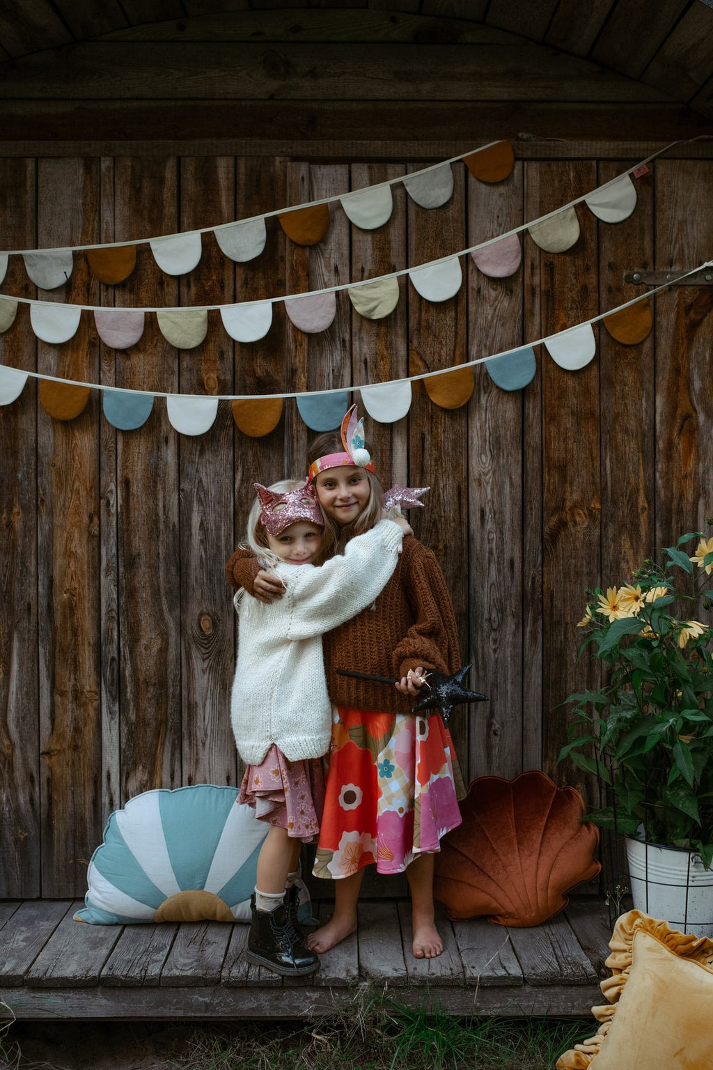1. Two children in costume, one wearing gold sequin cat mask, hugging in front of wooden backdrop