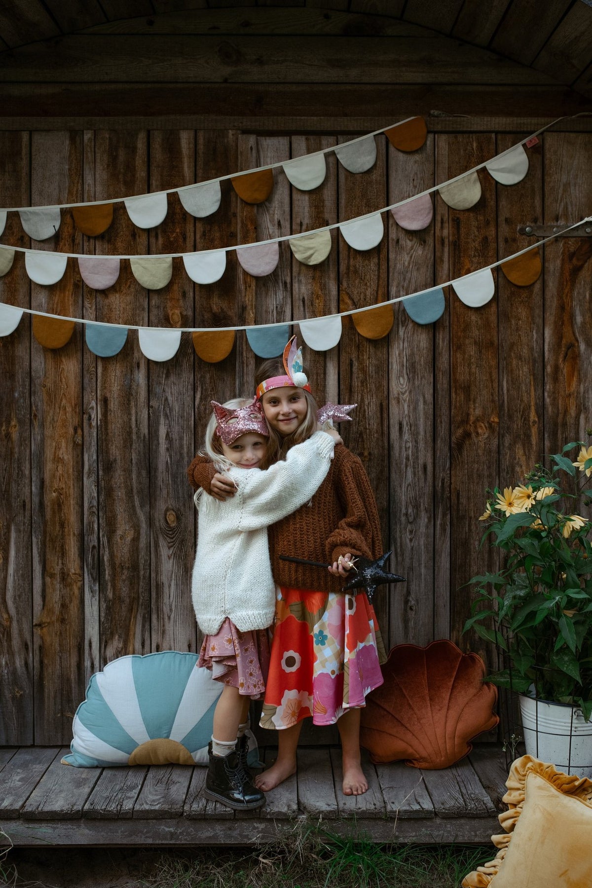 1. Two children in costume, one wearing gold sequin cat mask, hugging in front of wooden backdrop