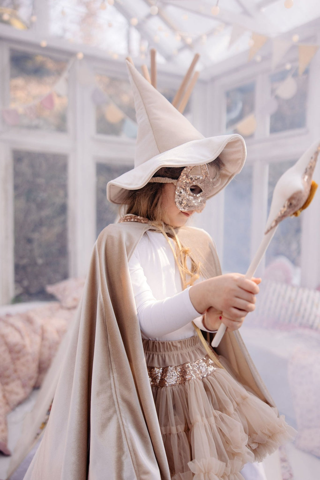 5. Girl in rose gold sequin cat mask and beige cape holding a wand in a decorated room