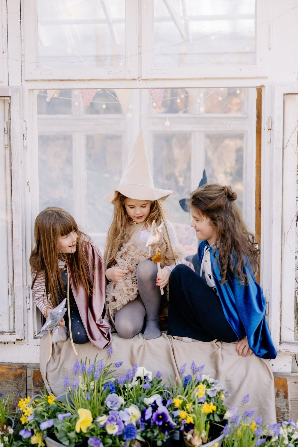 6. Three girls in costume sitting by a window with flowers, one wearing a rose gold cat mask