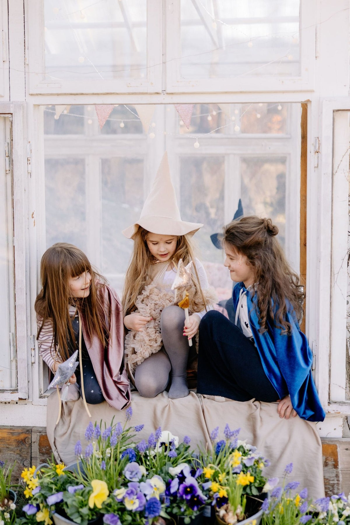 6. Three girls in costume sitting by a window with flowers, one wearing a rose gold cat mask