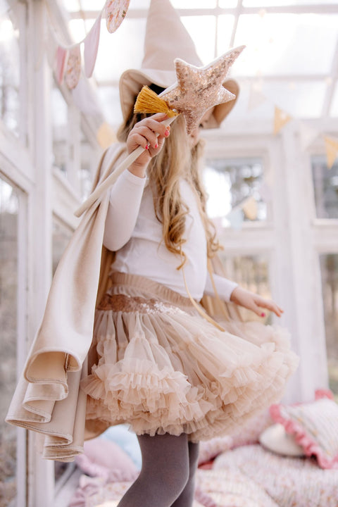 4. Girl in beige cape and tutu holding a star wand, standing in a bright room
