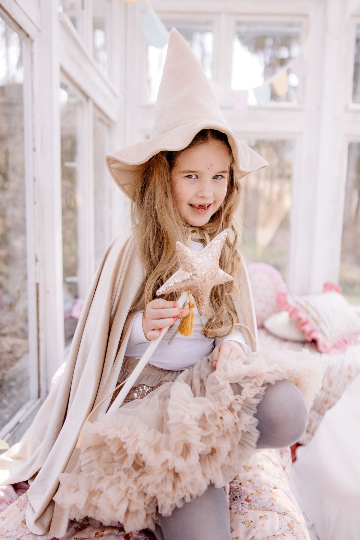 2. Girl in beige hat and tutu holding a star wand, sitting in a sunlit room