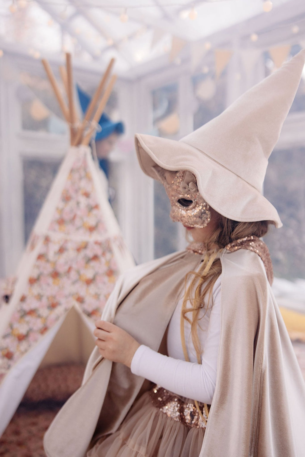 7. Girl in rose gold sequin cat mask and beige hat standing near a floral teepee