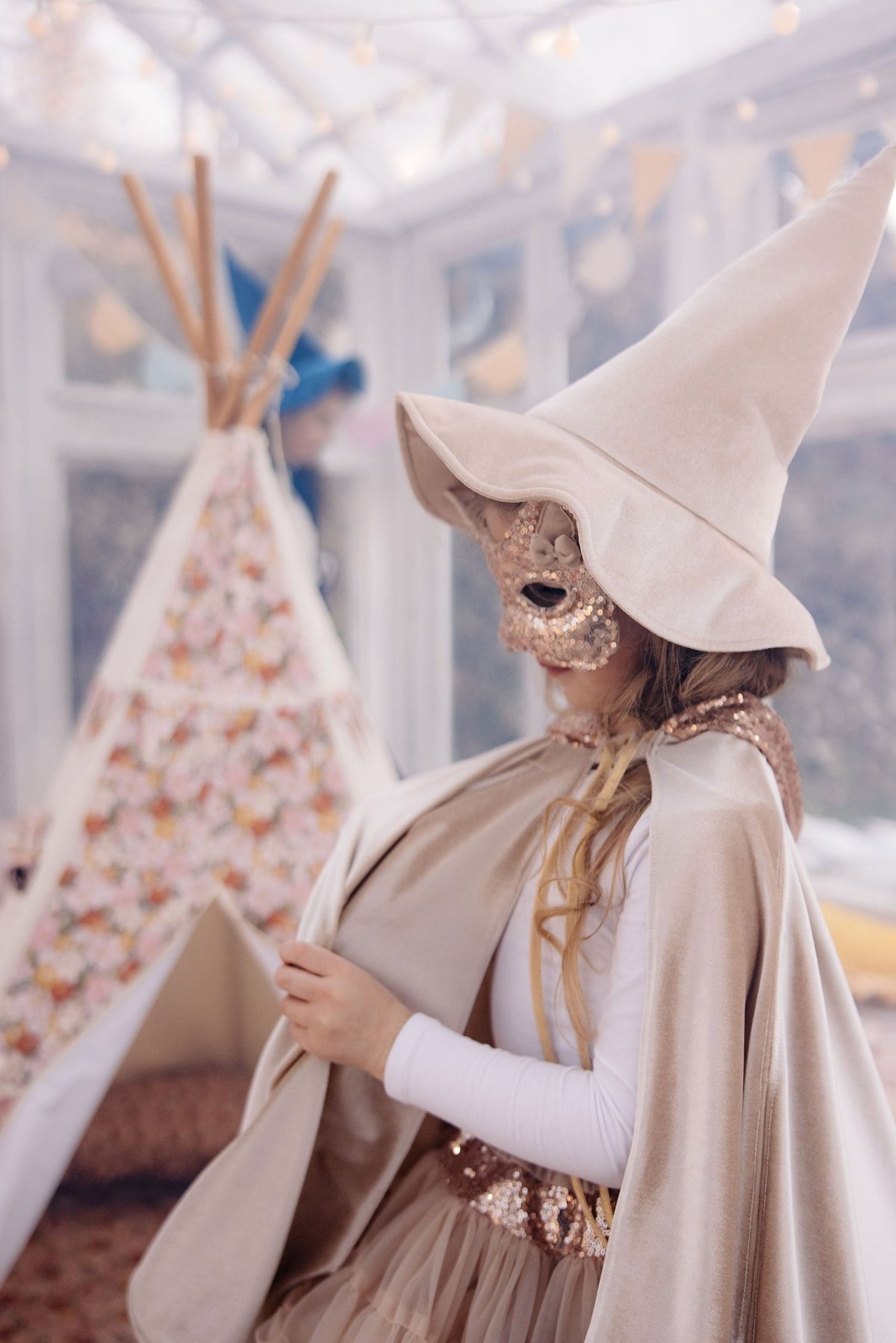 7. Girl in rose gold sequin cat mask and beige hat standing near a floral teepee