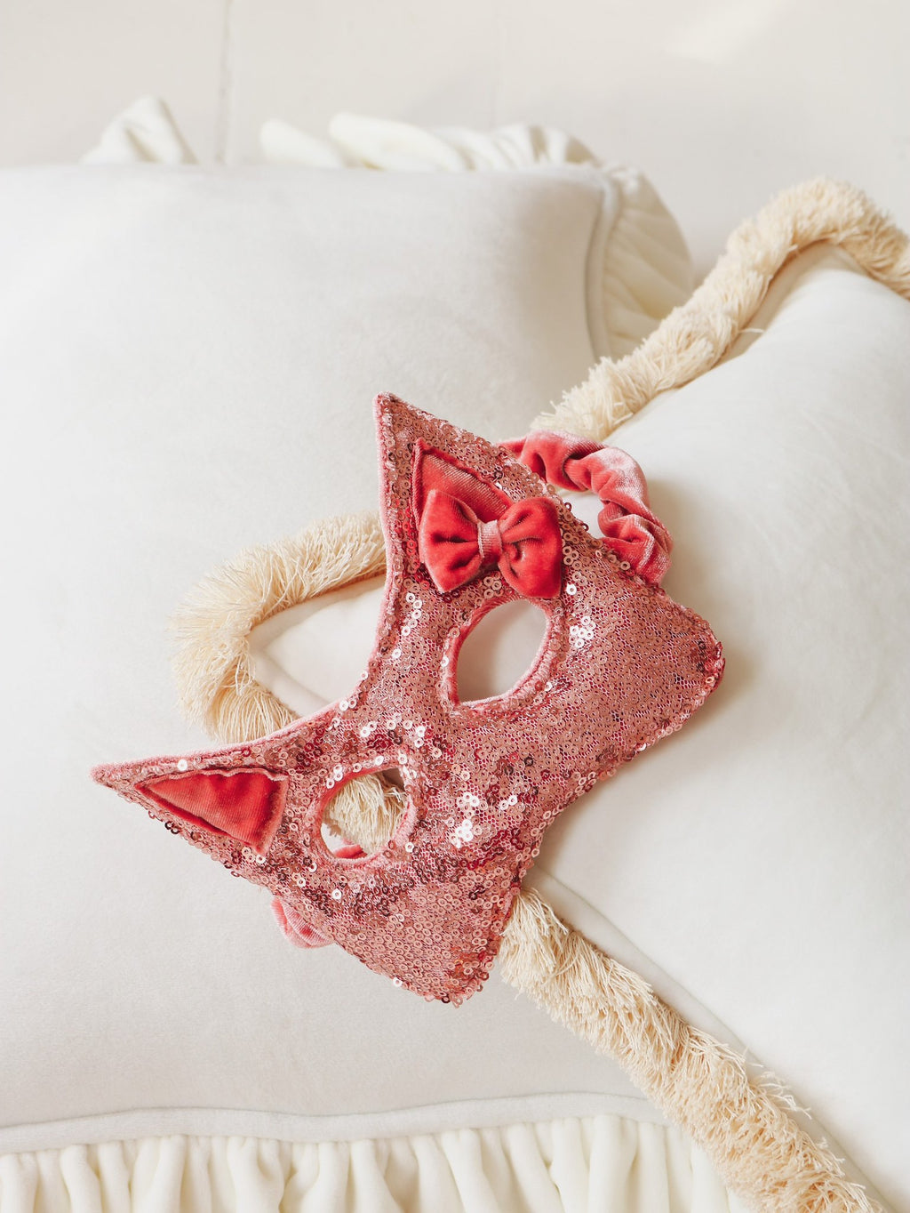 3. Close-up of pink sequin cat mask with velvet bow detail on white pillow background