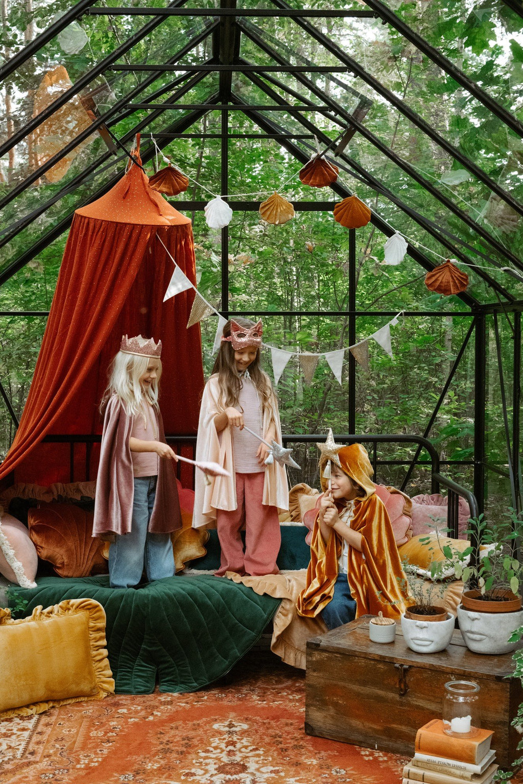 1. Three children in costume, one wearing pink sequin cat mask, playing in a decorated greenhouse