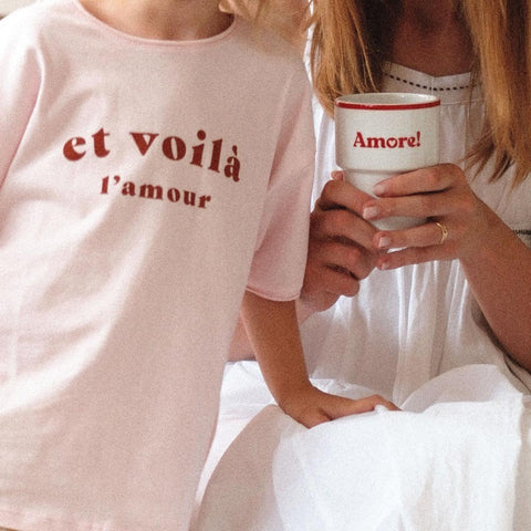 3. Woman and child with Terra Mamma Amore ceramic mug, red rim and 'Amore!' text, wearing casual clothing, in a relaxed home setting