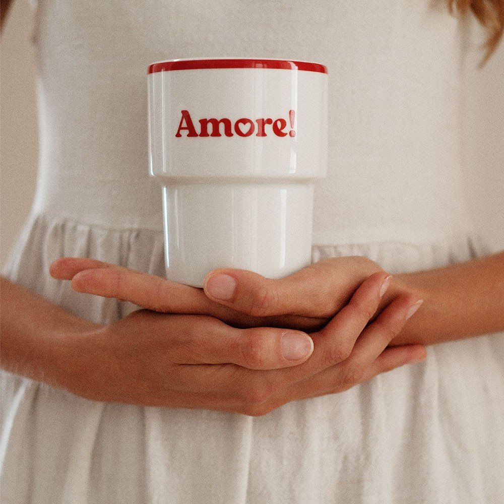 6. Woman in white dress holding Terra Mamma Amore ceramic mug with red rim and 'Amore!' text, close-up of hands