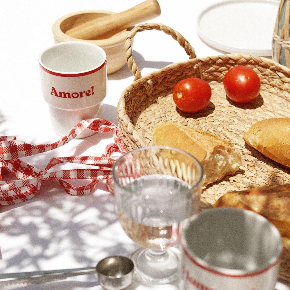 4. Terra Mamma Amore ceramic mug with red rim and 'Amore!' text on a table with bread, tomatoes, and woven basket, outdoor picnic setting