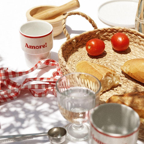 4. Terra Mamma Amore ceramic mug with red rim and 'Amore!' text on a table with bread, tomatoes, and woven basket, outdoor picnic setting