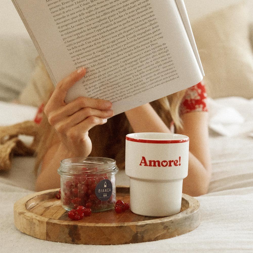 2. Terra Mamma Amore ceramic mug with red rim and 'Amore!' text on a wooden tray with berries, woman reading a book in bed