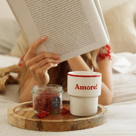 2. Terra Mamma Amore ceramic mug with red rim and 'Amore!' text on a wooden tray with berries, woman reading a book in bed